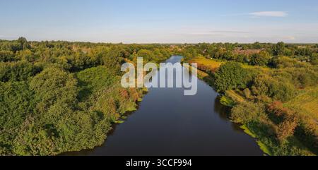 Veduta aerea di Woolston Weir sul fiume Mersey a Warrington, che mostra la struttura idroelettrica e lo spillway da lontano, circondato da lussureggianti Foto Stock