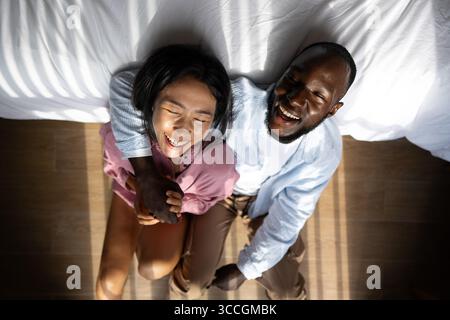 Giovani coppie diverse che sorridono gioiosamente insieme nel loro luminoso soggiorno, indossando abiti casual Foto Stock