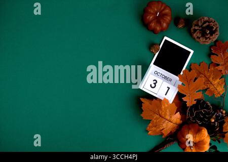Su uno sfondo verde si trova un calendario con la data di Halloween, circondato da paraphernalia autunnali.spazio per il testo. Foto Stock