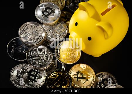 Un salvadanaio giallo circondato da monete Bitcoin in argento e oro su una superficie nera. L'immagine simboleggia la valuta digitale, i risparmi finanziari e l'inve Foto Stock