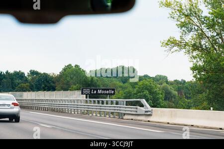 Alsazia, Francia - 24 agosto 2023: Vista dall'auto sull'autostrada francese che attraversa il fiume Mosella con foresta verde sullo sfondo e cartello indicante il fiume na Foto Stock