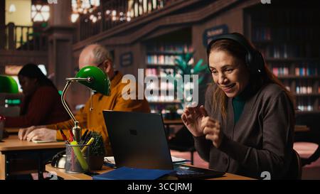 Una donna ascolta la musica ad alto volume con le cuffie e disturba le altre persone in biblioteca, un uomo anziano le chiede di mantenere basso il volume, violando le regole della biblioteca. Una persona disinteressata che canta. Foto Stock