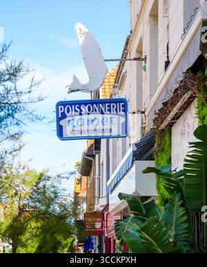 Le Touquet, Francia - 22 agosto 2023: Una strada vivace con il segno blu di Poissonnerie Ramet con una figura di pesce sopra, circondata dal verde, Foto Stock