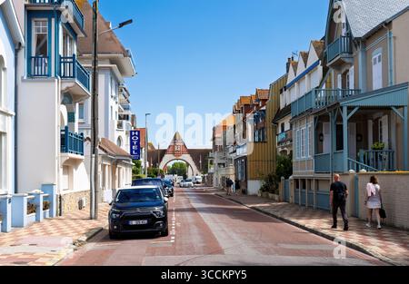 Le Touquet, Francia - 22 agosto 2023: Una strada soleggiata in , fiancheggiata da case colorate con balconi e persiane, mentre i pedoni camminano lungo il lato Foto Stock