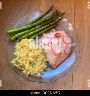 Un pasto a base di salmone, asparagi e couscous viene presentato su un piatto di vetro. Foto Stock