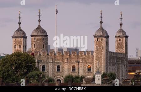 Vista della Torre di Londra al tramonto con bandiera abbassata, che mostra le storiche mura e torri di pietra contro un cielo nuvoloso a Londra, Regno Unito Foto Stock