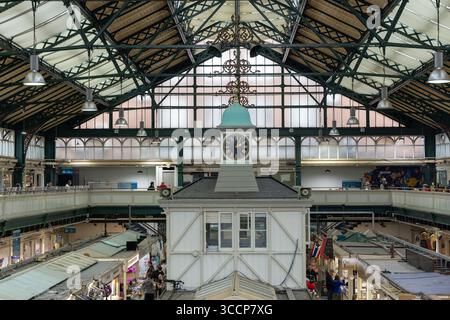 CARDIFF, Regno Unito - 8 AGOSTO 2025 - Torre dell'orologio con orologio analogico che mostra l'ora nel mercato interno di Cardiff in Galles, sotto il tetto in vetro e acciaio, con bancarelle A. Foto Stock