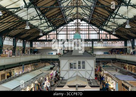 CARDIFF, Regno Unito - 8 AGOSTO 2025 - Vista interna del mercato di Cardiff, Galles, con la sua torre dell'orologio, le bancarelle e i clienti che acquistano prodotti locali Foto Stock
