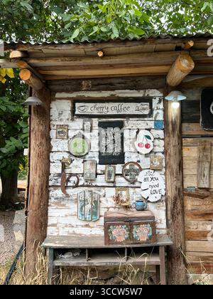 Angolo caffè rustico all'aperto con insegne vintage e tessuti in legno, che creano un'atmosfera accogliente di campagna. Foto Stock
