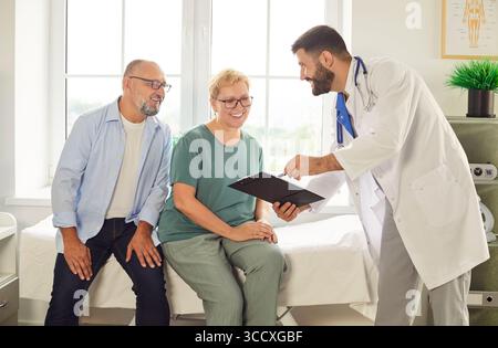 Sorridente senior coppia consulenza con medico amichevole in luminoso ufficio medico Foto Stock