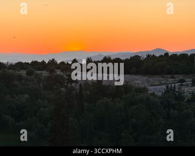 I colori del tramonto dipingono il cielo sopra Atene, visto dalla collina di Areopago con l'Acropoli e il colle di Licabetto sullo sfondo. Foto Stock