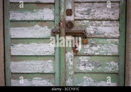Una vecchia porta di legno intemprata con una serratura arrugginita Foto Stock