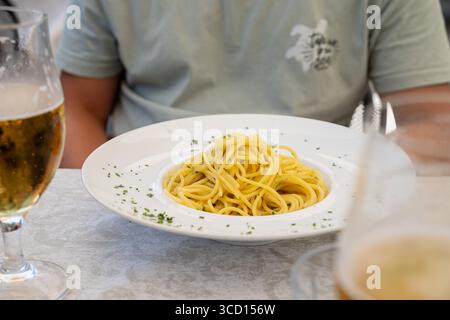 Limone, Lago di Garda, Italia 7 agosto 2025: Spaghetti aglio e olio pasta classica con aglio, olio d'oliva e peperoncino in un ristorante con un ospite e birra. *** Spaghetti aglio e olio klassische Pasta mit Knoblauch, Olivenöl und peperoncino im Restaurant mit Gast und Bier. Foto Stock