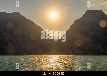 Italia - 7 agosto 2025: Tra Limone e Riva del Garda, il sole tramonta sul Lago di Garda. La luce dorata si riflette sulle onde e le montagne diventano sagome. *** Zwischen Limone und Riva del Garda sinkt die Sonne über dem Gardasee. Goldenes Licht spiegelt auf den Wellen, Die Berge werden zu Silhouetten. Foto Stock