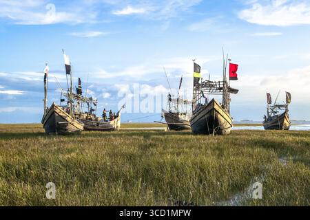 Chattogram, Bangladesh - 19 settembre 2023: Vista delle barche da pesca che riposano sulla riva erbosa, le loro bandiere colorate sventolano dolcemente nella brezza sotto un vasto cielo striato di nuvole. Foto Stock