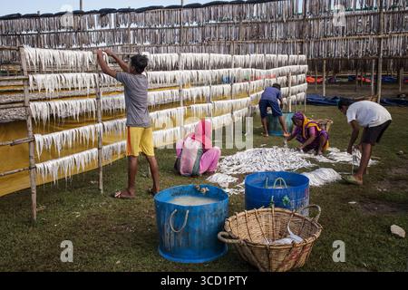 Cox's Bazar, Bangladesh - 29 novembre 2022: Vista dei lavoratori che impiccano e selezionano i pesci su rack di bambù, creando un netto contrasto bianco contro l'eart Foto Stock