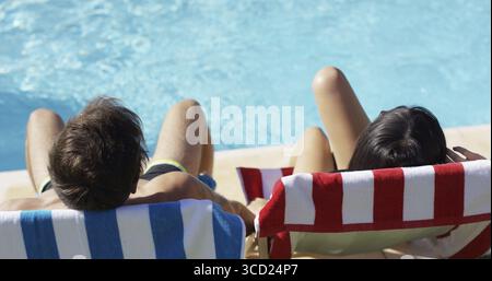 Coppie che si rilassano su sedie a sdraio colorate presso la piscina godendosi la calda vista del sole estivo dal retro con solo la testa visibile Foto Stock