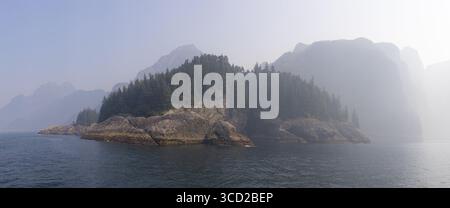 Vista delle isole rocciose che si innalzano dalle acque della Resurrection Bay, coronate da fitte foreste verdi scure sullo sfondo di montagne torreggianti e nebbiose Foto Stock