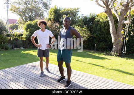 Diversi amici maschili in abbigliamento sportivo in piedi sul ponte nel cortile a controllare i tracker vicino alle corde dello swing Foto Stock