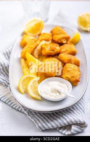 Pesce e patatine tradizionali con salsa al limone e tartaro sul piatto da portata Foto Stock