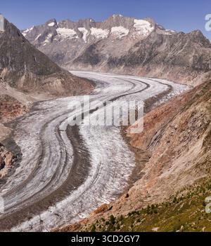 La vista aerea del maestoso ghiacciaio Aletsch scolpì il suo percorso ghiacciato attraverso aspre montagne baciate dal sole, una danza di ghiaccio bianco-blu contro i marroni della terra, Foto Stock