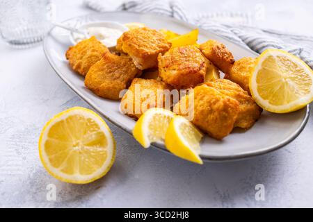 Pesce e patatine tradizionali con salsa al limone e tartaro sul piatto da portata Foto Stock