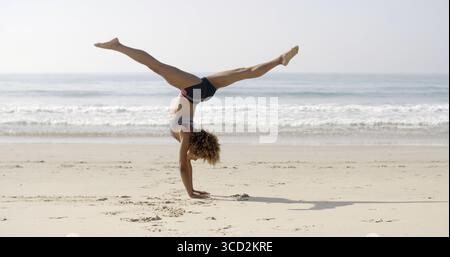 Giovane donna che fa il cartoncino sulla spiaggia con un mare calmo sullo sfondo Foto Stock