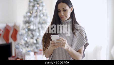Giovane donna attraente che legge un messaggio di testo sul suo telefono cellulare con un sorriso tranquillo, ravvicinato la testa e le spalle ad angolo basso Foto Stock