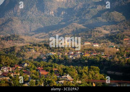 Tempio buddista dorato che si affaccia sui tradizionali tetti di Luang Prabang, sul Laos al tramonto con sfondo della Foresta di montagna Foto Stock