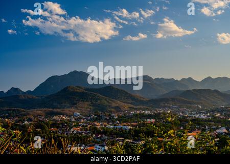 Vista panoramica aerea di Luang Prabang, Laos con tetti tradizionali e Montagne Rive sotto il cielo azzurro al tramonto Foto Stock