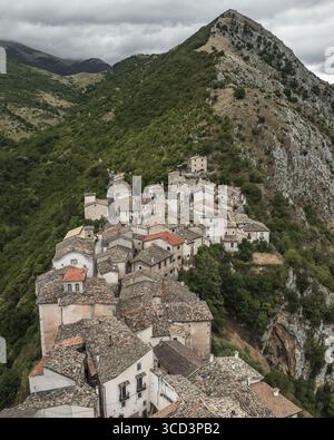 Veduta aerea di antiche abitazioni raggruppate saldamente insieme, aggrappate alla ripida collina sotto una maestosa vetta di montagna, Castrovalva, Abruzzo, Italia. Foto Stock