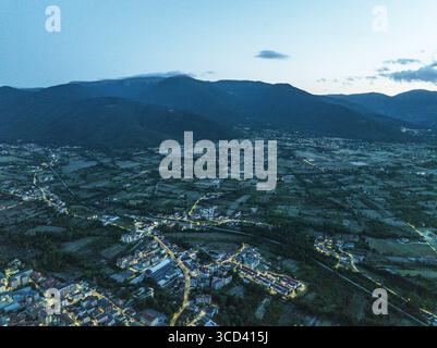 Vista aerea della tranquilla cittadina incastonata tra le montagne, con le luci che brillano dolcemente contro il verde scuro paesaggio di Sulmona, Abruzzo, Italia. Foto Stock