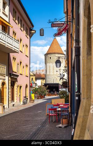Yverdon les Bains, Svizzera - 24 luglio 2025: Una pittoresca strada di Yverdon, edifici colorati, un sentiero acciottolato e una torre storica nel b Foto Stock