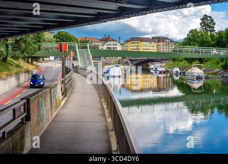 Yverdon les Bains, Svizzera - 24 luglio 2025: Vista sul canale delle barche, ponte pedonale verde e riflessi sull'acqua. L'area circostante include Foto Stock