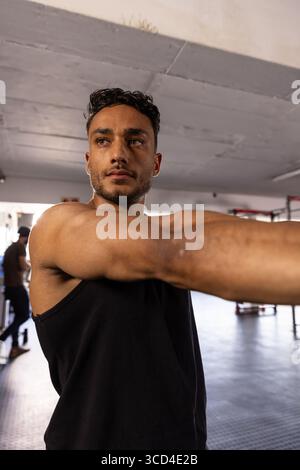 Uomo ventenne che indossa una canotta che si allunga con le braccia in avanti sui portapacchi della palestra Foto Stock