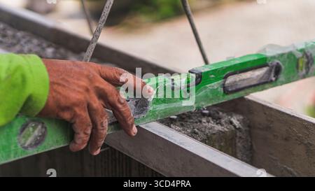 Una livella a bolla d'aria si appoggia sul calcestruzzo per garantire l'uniformità della superficie, un passo essenziale per mantenere precisione e qualità nei lavori di costruzione Foto Stock