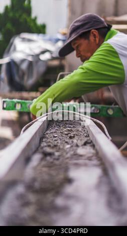Una livella a bolla d'aria si appoggia sul calcestruzzo per garantire l'uniformità della superficie, un passo essenziale per mantenere precisione e qualità nei lavori di costruzione Foto Stock