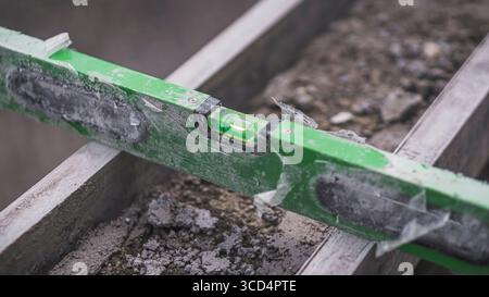 Una livella a bolla d'aria si appoggia sul calcestruzzo per garantire l'uniformità della superficie, un passo essenziale per mantenere precisione e qualità nei lavori di costruzione Foto Stock