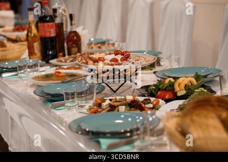 Un tavolo da banchetto splendidamente organizzato presenta una selezione di salumi, antipasti freschi, piatti turchesi e bottiglie di vino su un fresco tavolo bianco Foto Stock