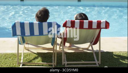Coppie che si rilassano su sedie a sdraio colorate presso la piscina godendosi la calda vista del sole estivo dal retro con solo la testa visibile Foto Stock
