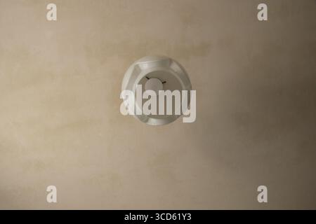 Lampada da soffitto con paralume rotondo bianco e lampadina in una stanza con vecchie riparazioni e intonaco leggero in un appartamento Foto Stock