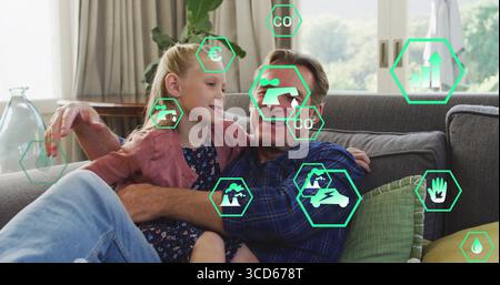Nonno e nipote seduti sul divano grigio nel soggiorno, mostrando icone ecologiche esagonali Foto Stock