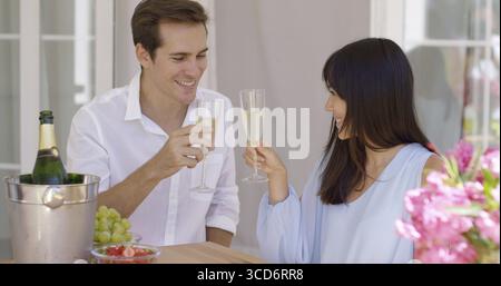 Coppia giovane e felice che brinda bicchieri di champagne per celebrare qualcosa di importante Foto Stock