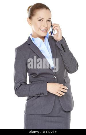 Una giovane donna d'affari felice con un sorriso che sta in piedi a chiacchierare sul suo cellulare isolato sul bianco Foto Stock