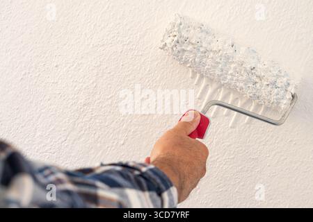 Primo piano di una mano. Un pittore dipinge una parete in muratura con vernice bianca utilizzando un rullo. Industria edile. Foto Stock