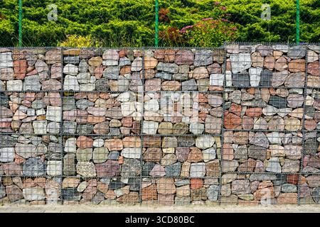 Primo piano di una parete in gabbione realizzata in pietre naturali colorate in una rete metallica, utilizzata per la progettazione paesaggistica e il controllo dell'erosione Foto Stock