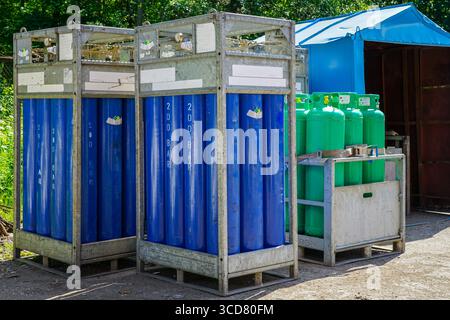 Bombole di gas industriali blu e verdi conservate in rack metallici in una struttura esterna, seguendo gli standard di sicurezza e pressione per l'uso industriale Foto Stock