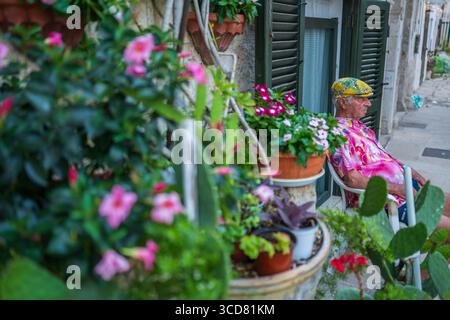 Uomo maturo seduto fuori da una casa decorata con numerose piante e vasi, Monopoli, Italia Foto Stock