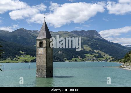 La torre della chiesa sommersa nel lago di Resia sullo sfondo alpino Foto Stock