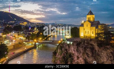 Il centro e la città vecchia di Tbilisi, la chiesa di Metekhi sulla collina sul fiume Kura. Parte del ponte pedonale 'Peace' e del Vahtang King Gorgasali equestre Foto Stock